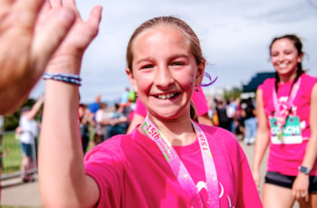 Girls on the Run Coach and participant both smile while holding hands at 5K 